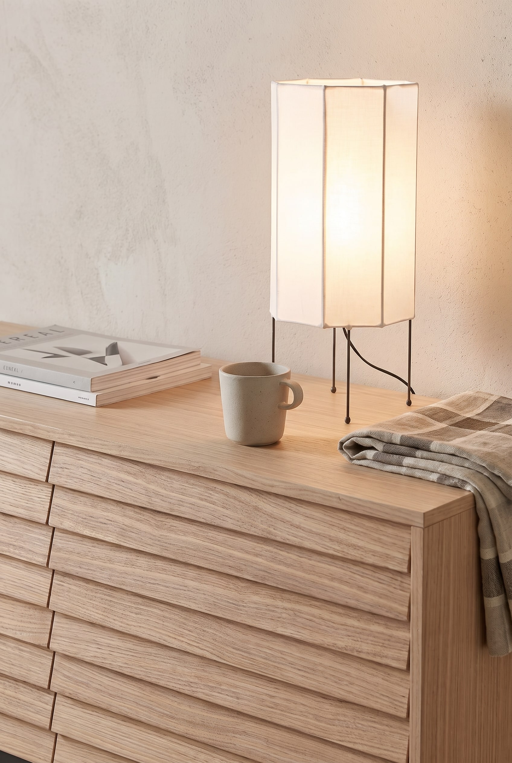 Gros plan d'un sideboard clair en bois de frêne avec une structure à lamelles verticales, décoré d'une délicate lampe en papier et d'un vase en verre.