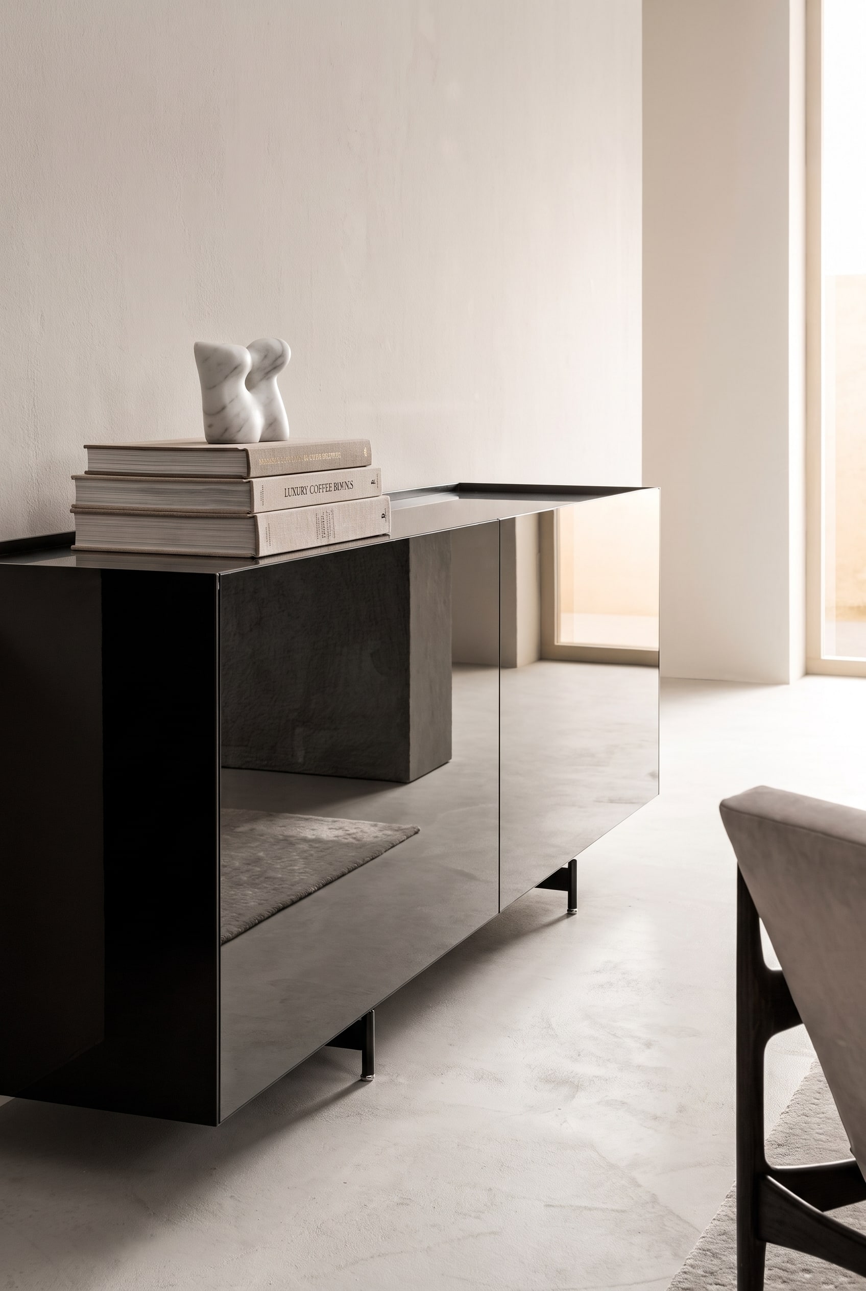 Sideboard avec façades miroir, surmonté d'une pile ordonnée de trois grands livres d'art, couronnée d'une petite sculpture en marbre blanc