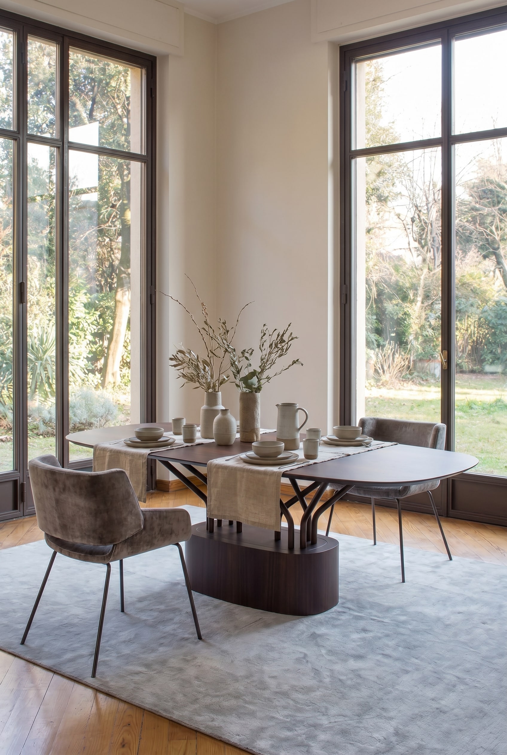 Salle &agrave; manger moderne avec une table en bois distinctive dont les pieds forment une structure en treillis ouverte, accompagn&eacute;e de chaises rembourr&eacute;es grises