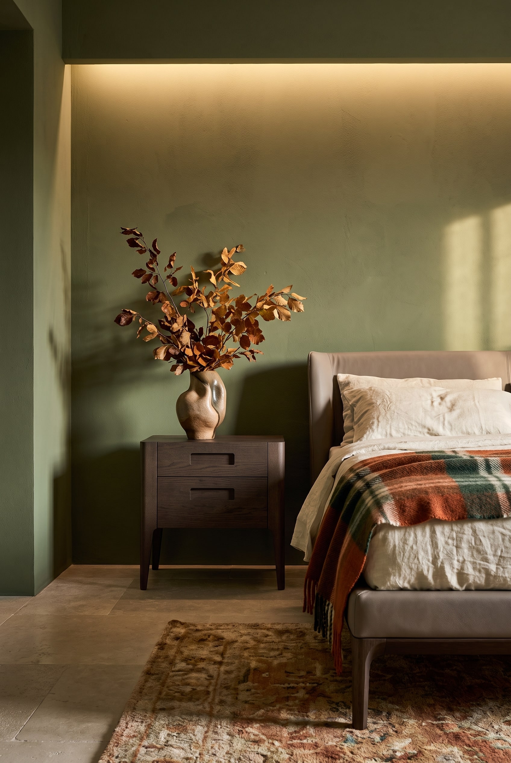 Une table de chevet en noyer fonc&eacute; &agrave; deux tiroirs se dresse avec style devant un mur vert olive mat dans une &eacute;l&eacute;gante chambre d'automne.