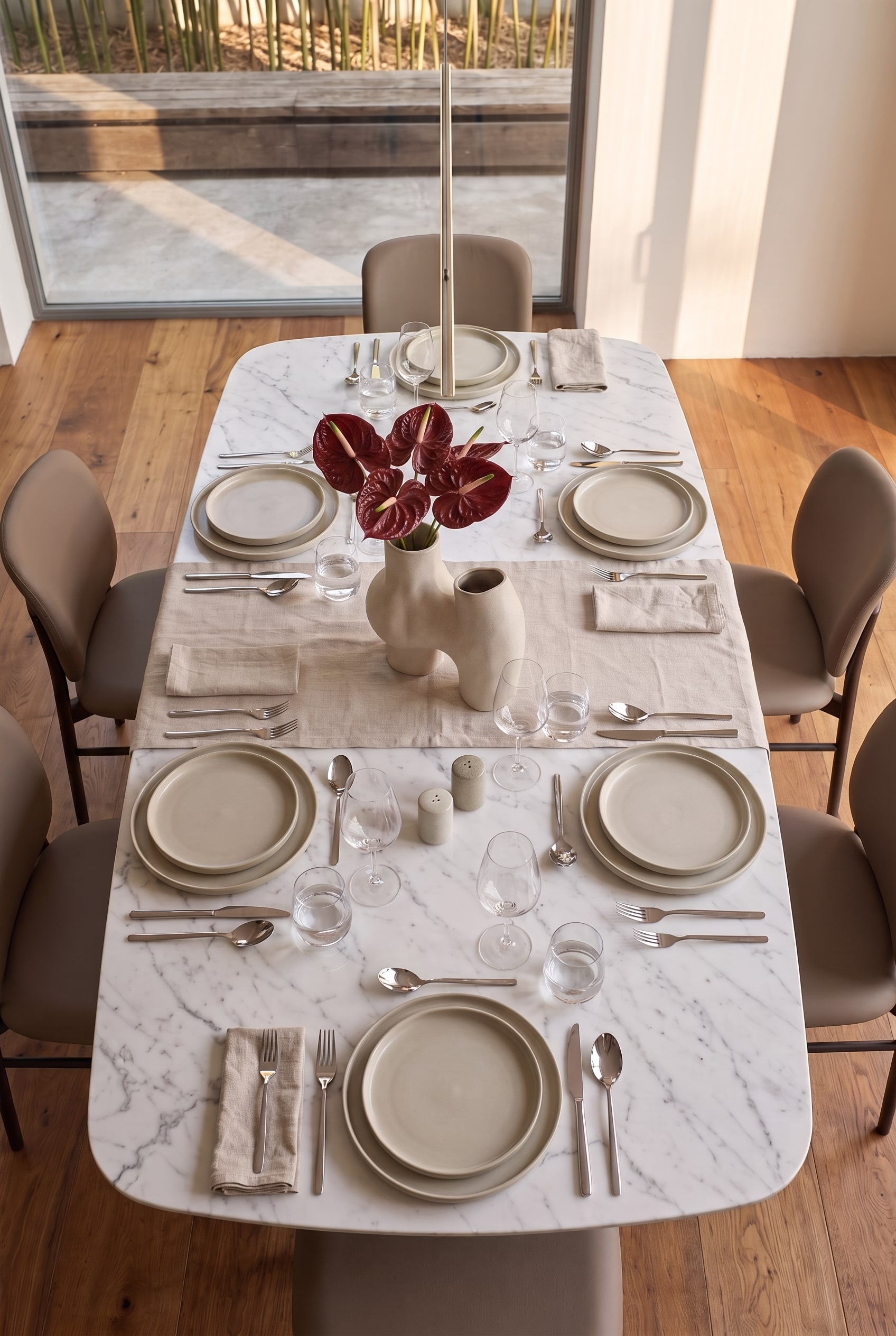 Vue plongeante sur une table &agrave; manger moderne dress&eacute;e pour six personnes avec chemin de table en lin, vaisselle en c&eacute;ramique et vase sculptural.