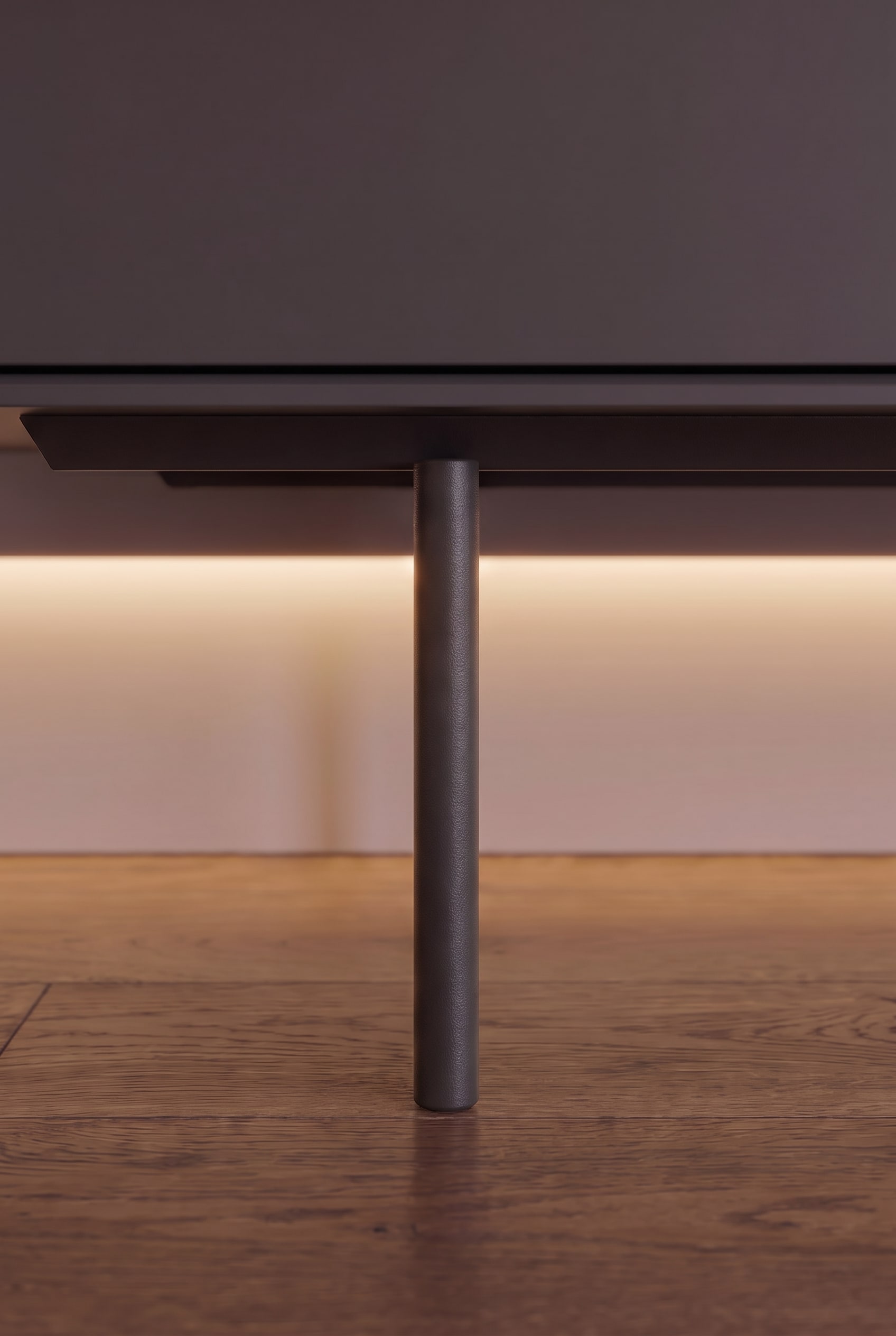 Gros plan d'un pied métallique cylindrique étroit d'un buffet avec éclairage indirect sous le meuble sur parquet en bois.