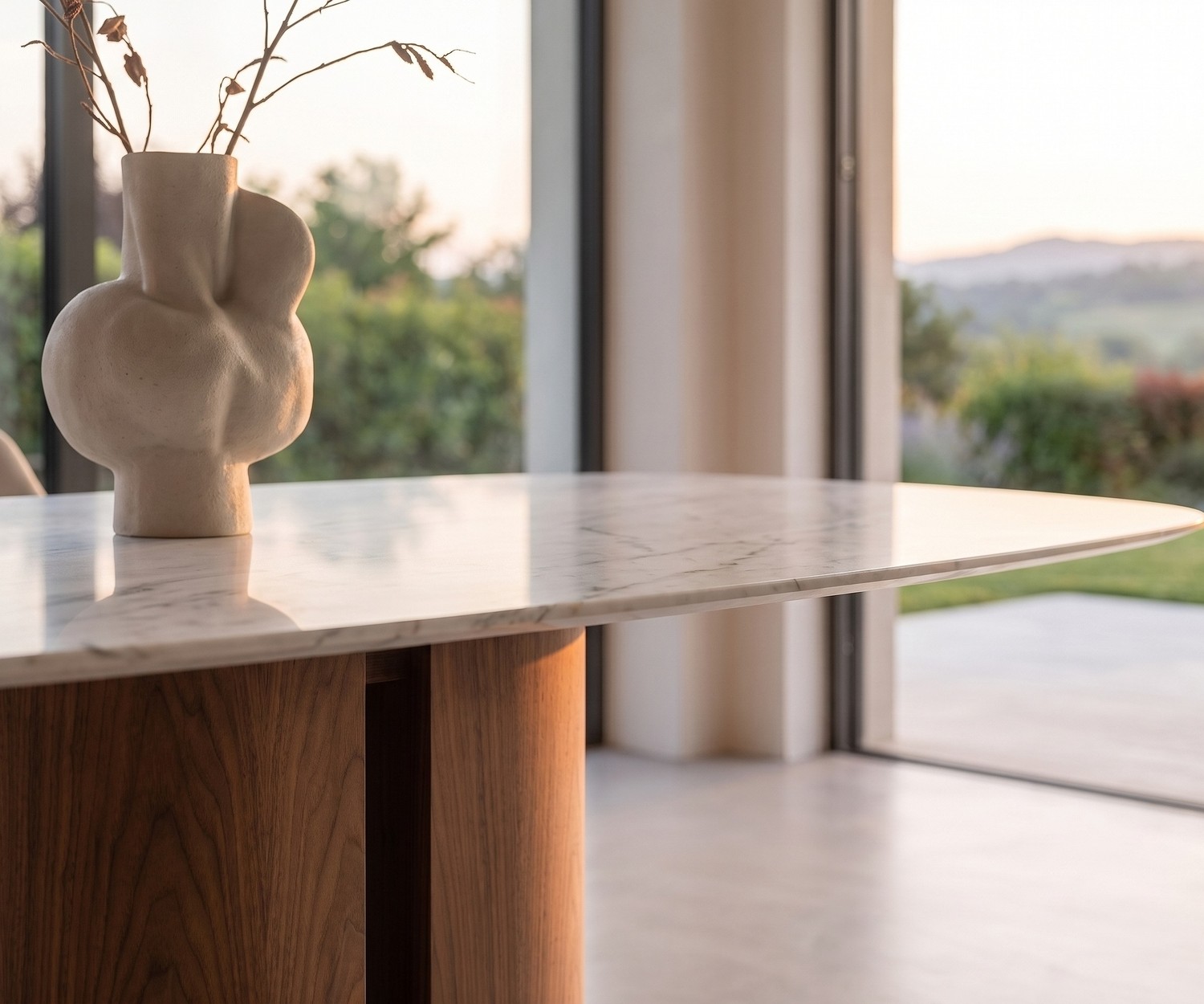 al2 el-it c 001 eettafel in een moderne eetkamer met wit marmerlook blad, houten zuilvoet en decoratieve vaas.