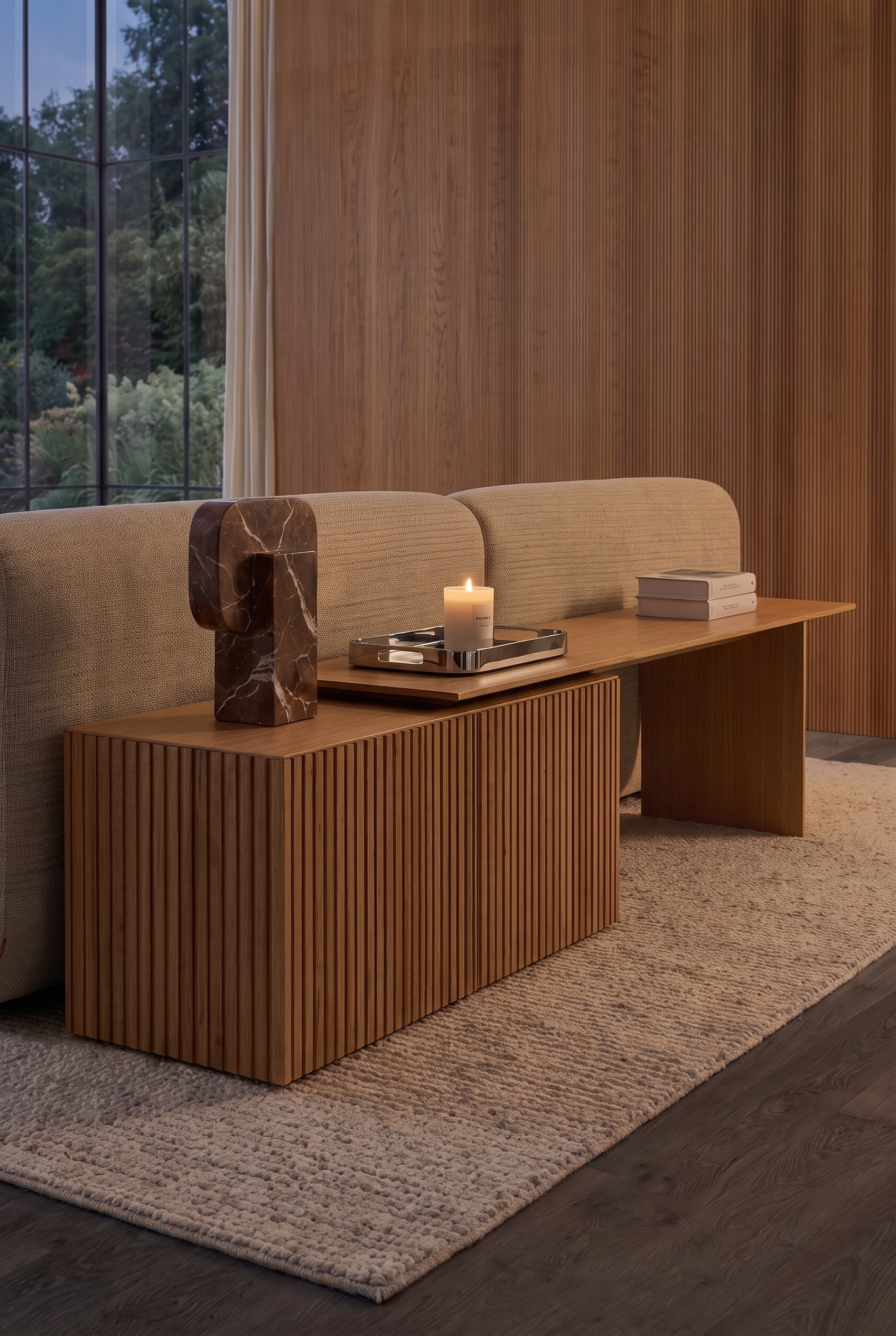 Vue d&eacute;taill&eacute;e du sideboard derri&egrave;re le canap&eacute;. On y voit le profil rainur&eacute;, un plateau avec une bougie allum&eacute;e et un objet en marbre.