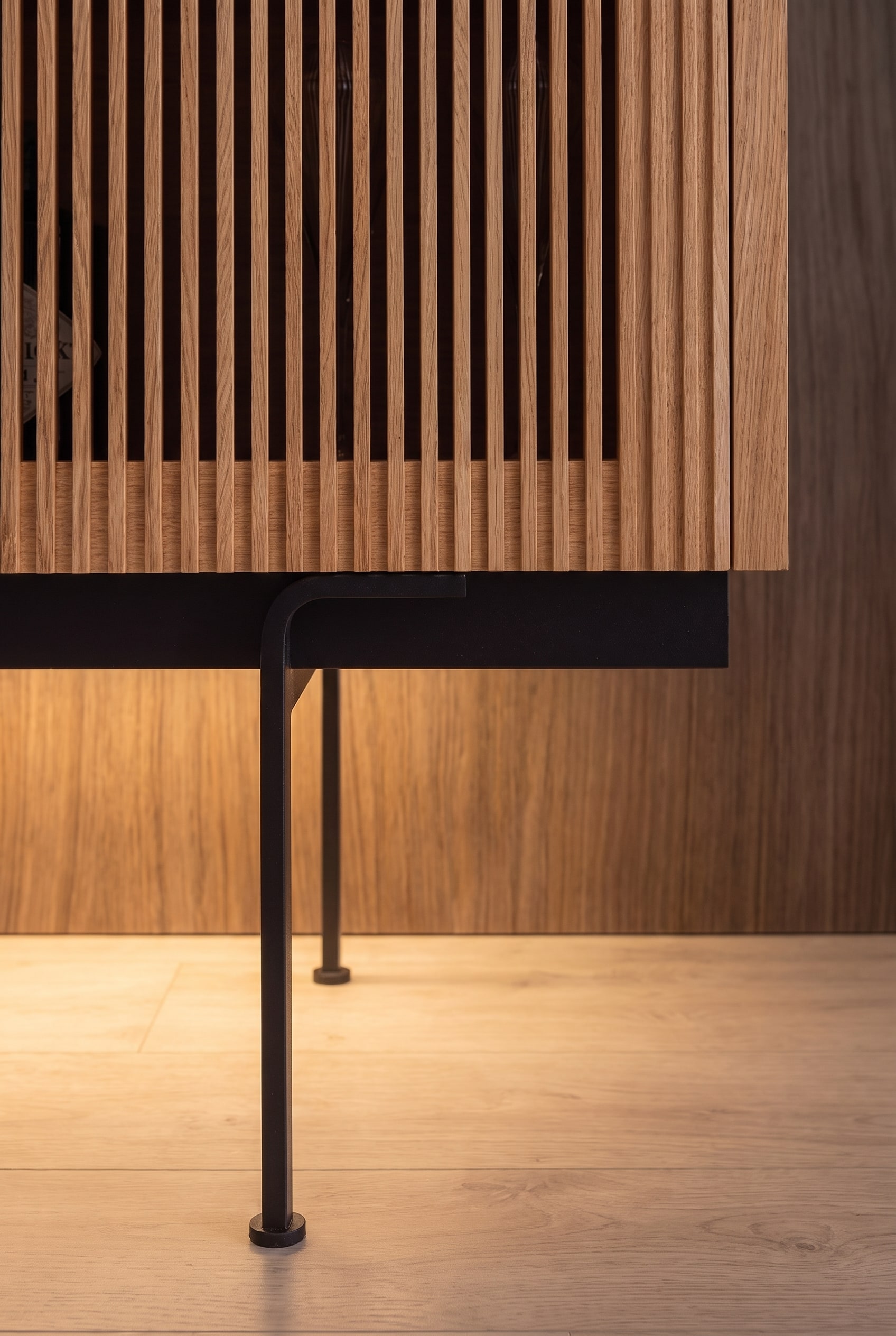 Detailaufnahme des schwarzen Metallbeins eines Highboards mit warmer indirekter Fu&szlig;bodenbeleuchtung.