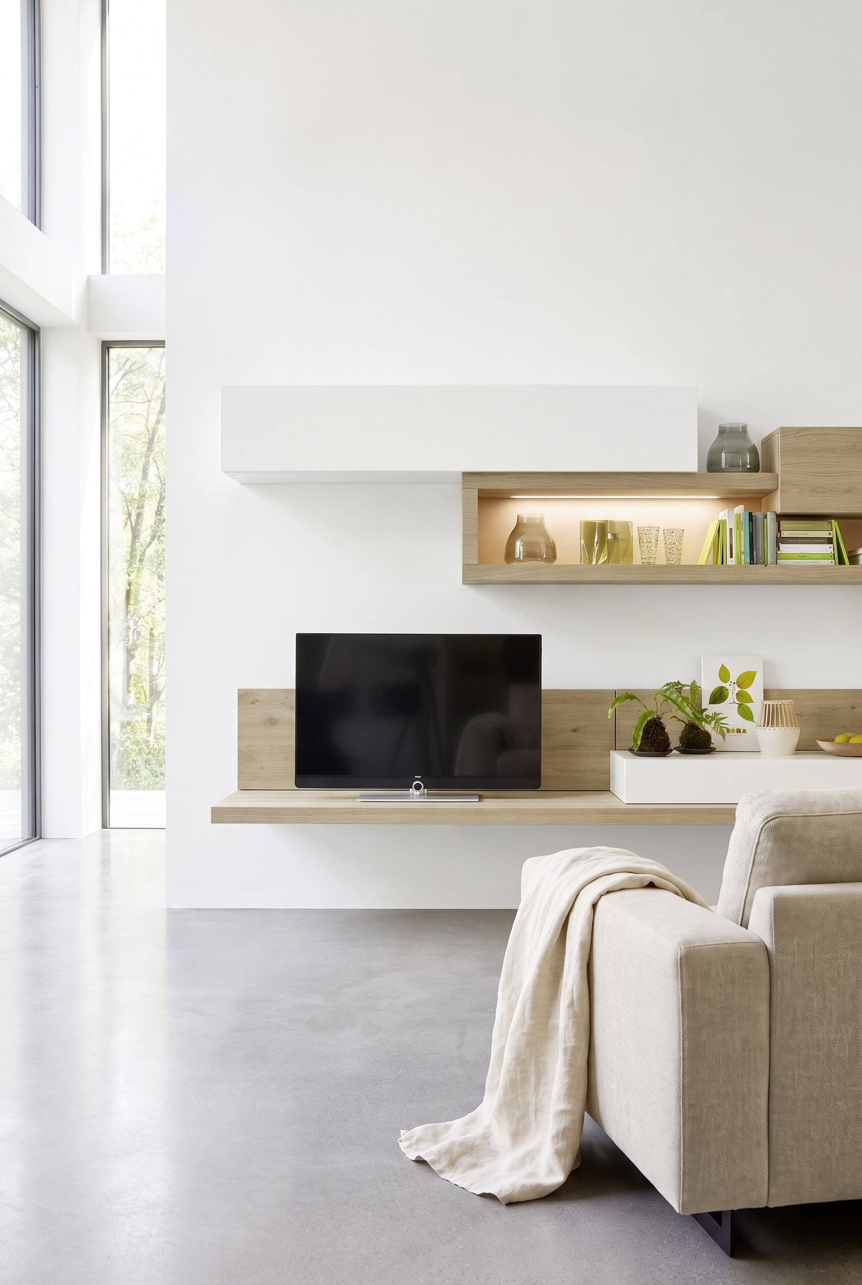 Meuble TV bas moderne en bois aspect chêne sauvage devant un mur en béton froid, combiné avec un plaid en lin texturé.