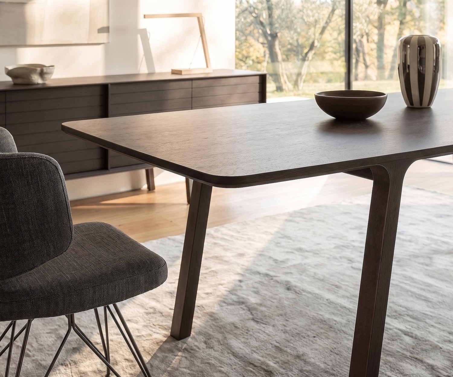Eettafel mobius 001 van al2 in donker eucalyptus hout in een moderne eetkamer met bijpassende designstoel en licht tapijt.