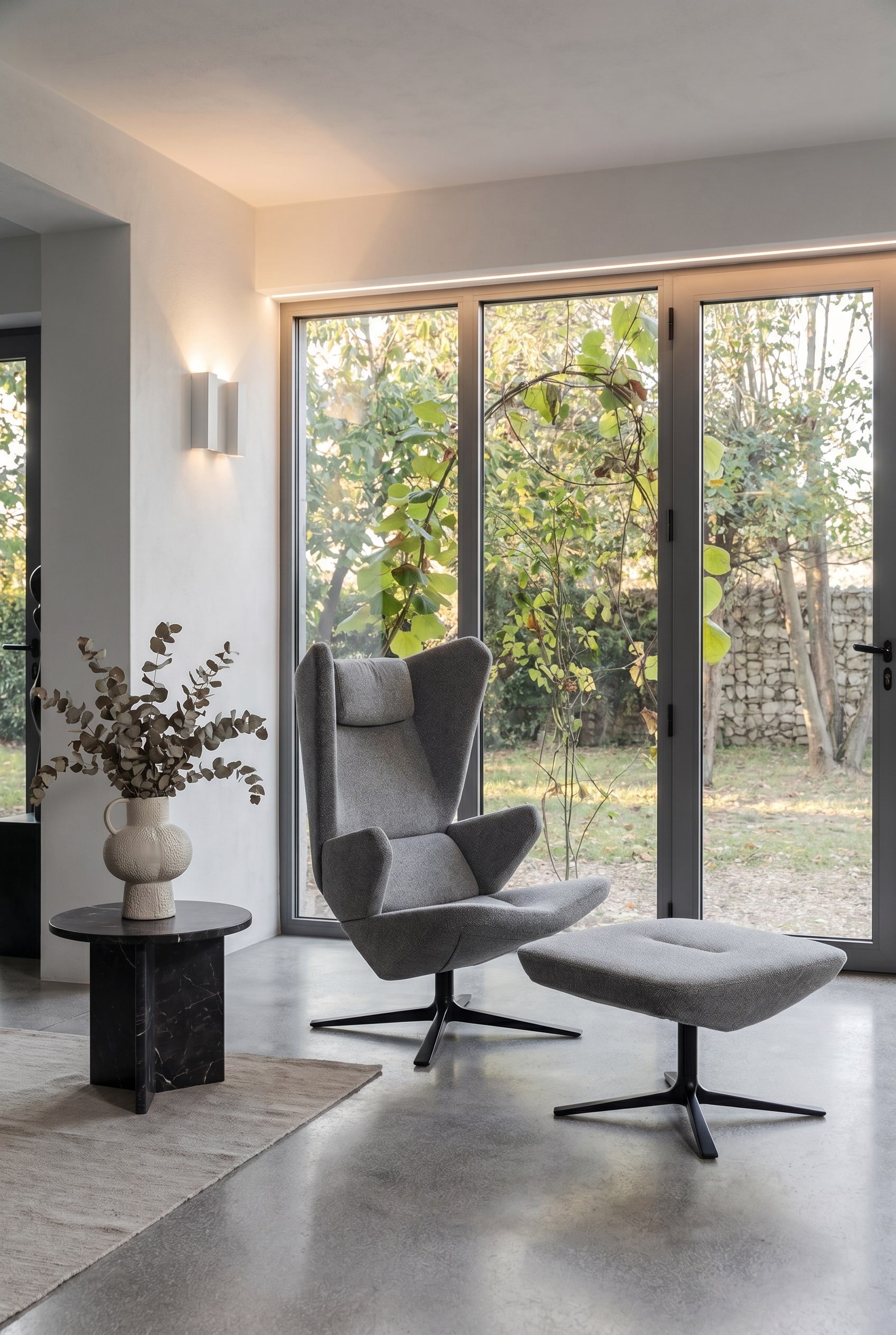 Salon moderne avec fauteuil Trifidae en tissu structur&eacute; gris, table d'appoint avec vase en c&eacute;ramique et grandes fen&ecirc;tres