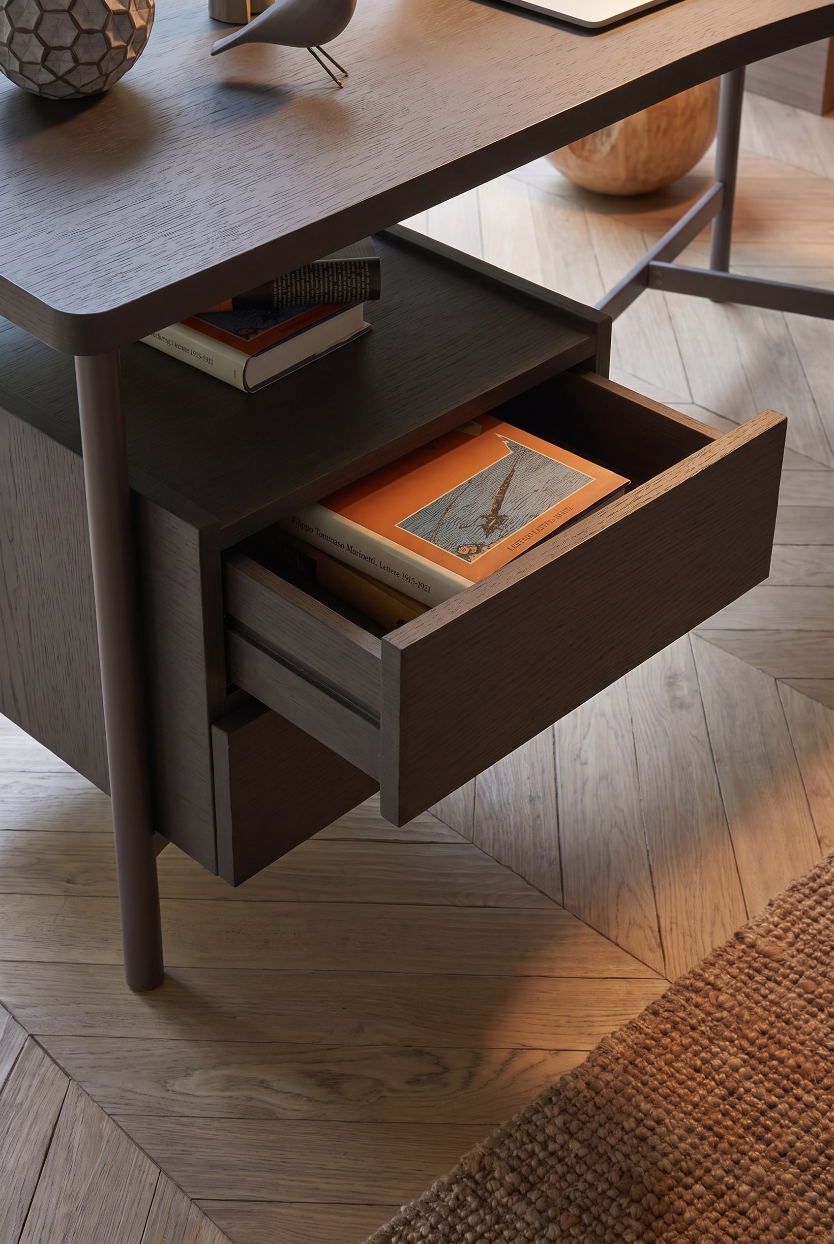 Tiroir affleurant ouvert du bureau en chêne foncé avec des livres rangés.