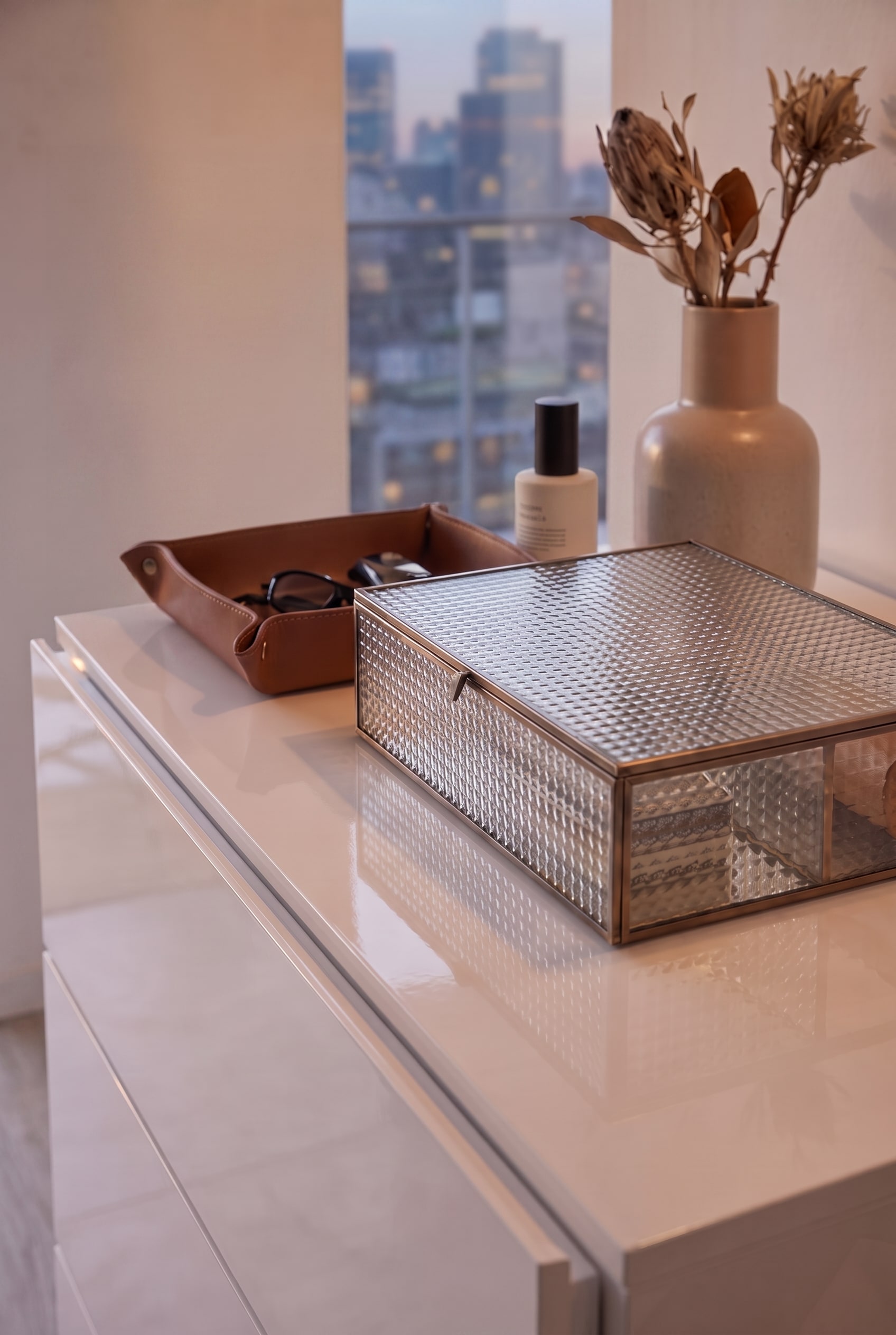 Vue de dessus d'une commode blanche brillante avec bo&icirc;te en verre et plateau en cuir, mise en sc&egrave;ne de mani&egrave;re puriste sans tringle &agrave; v&ecirc;tements.