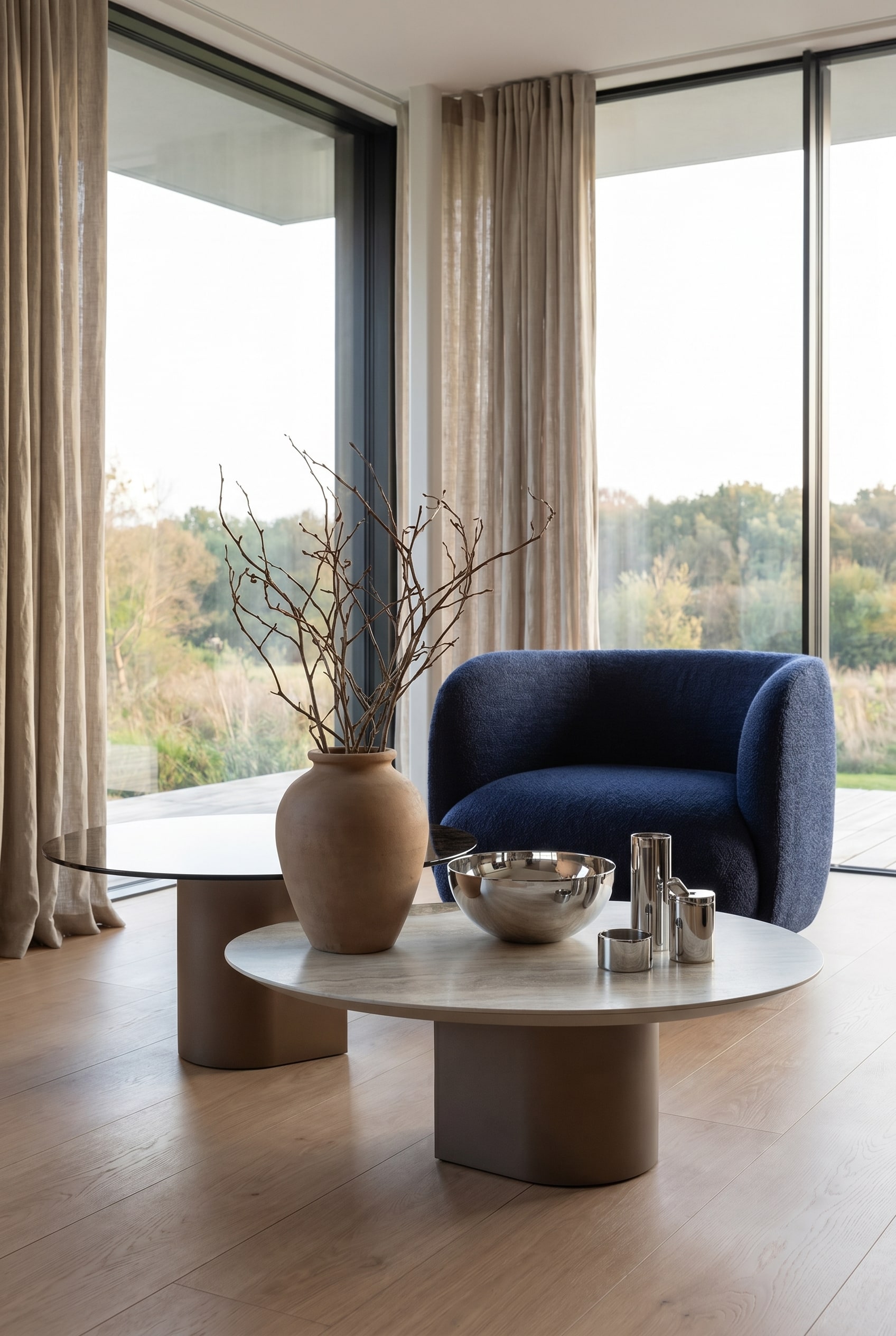 Salon avec table basse sculpturale, décoré d'un vase en argile mat, de branches sèches et d'une coupelle en acier inoxydable poli