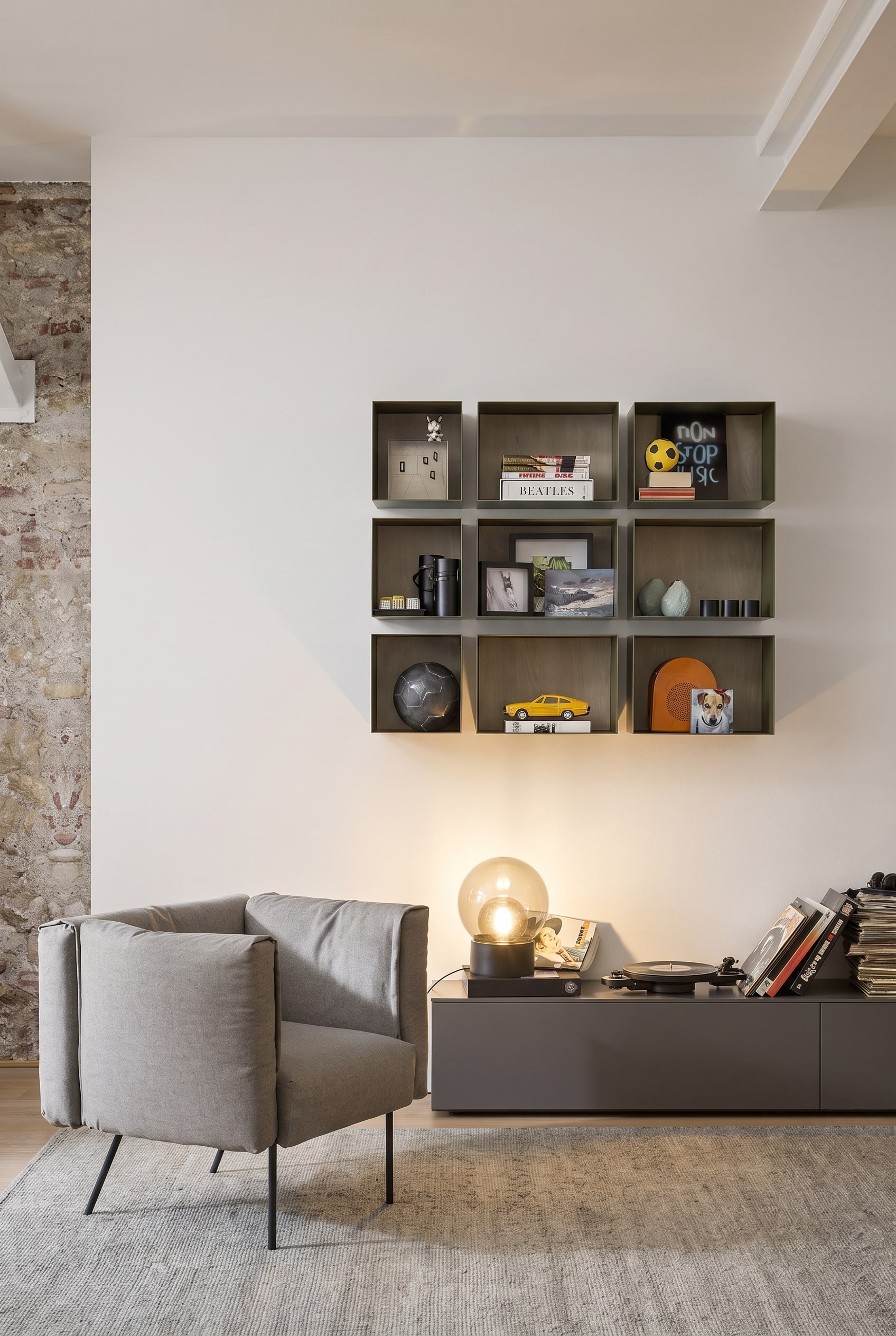 Minimalistische Leseecke mit schwebenden schwarzen Metall-Wandboxen, die mit B&uuml;chern gef&uuml;llt sind, und einem organisch geformten Sessel.