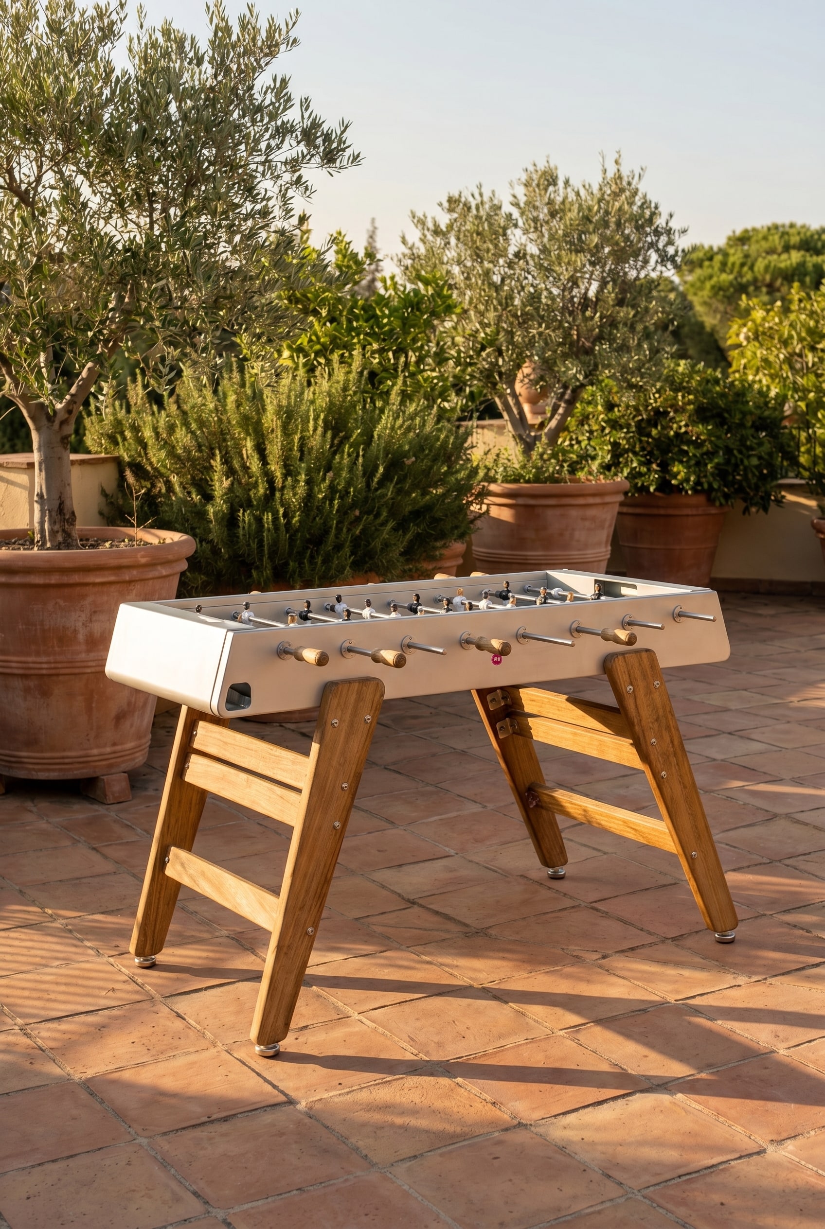 Terrasse méditerranéenne avec baby-foot en bois d'iroko et grandes jardinières sous la douce lumière du soir