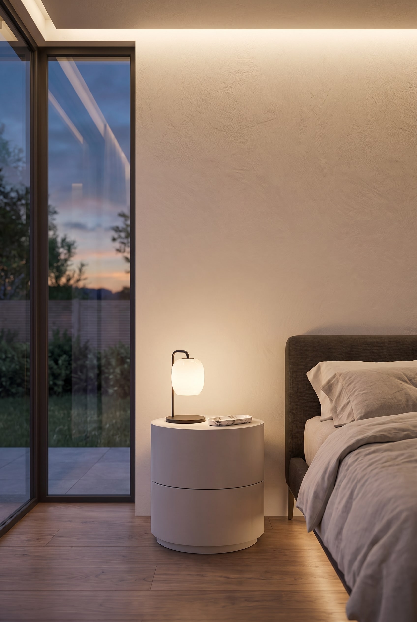 Table de chevet cylindrique et mate avec deux tiroirs, placée directement à côté d'un lit rembourré moderne.