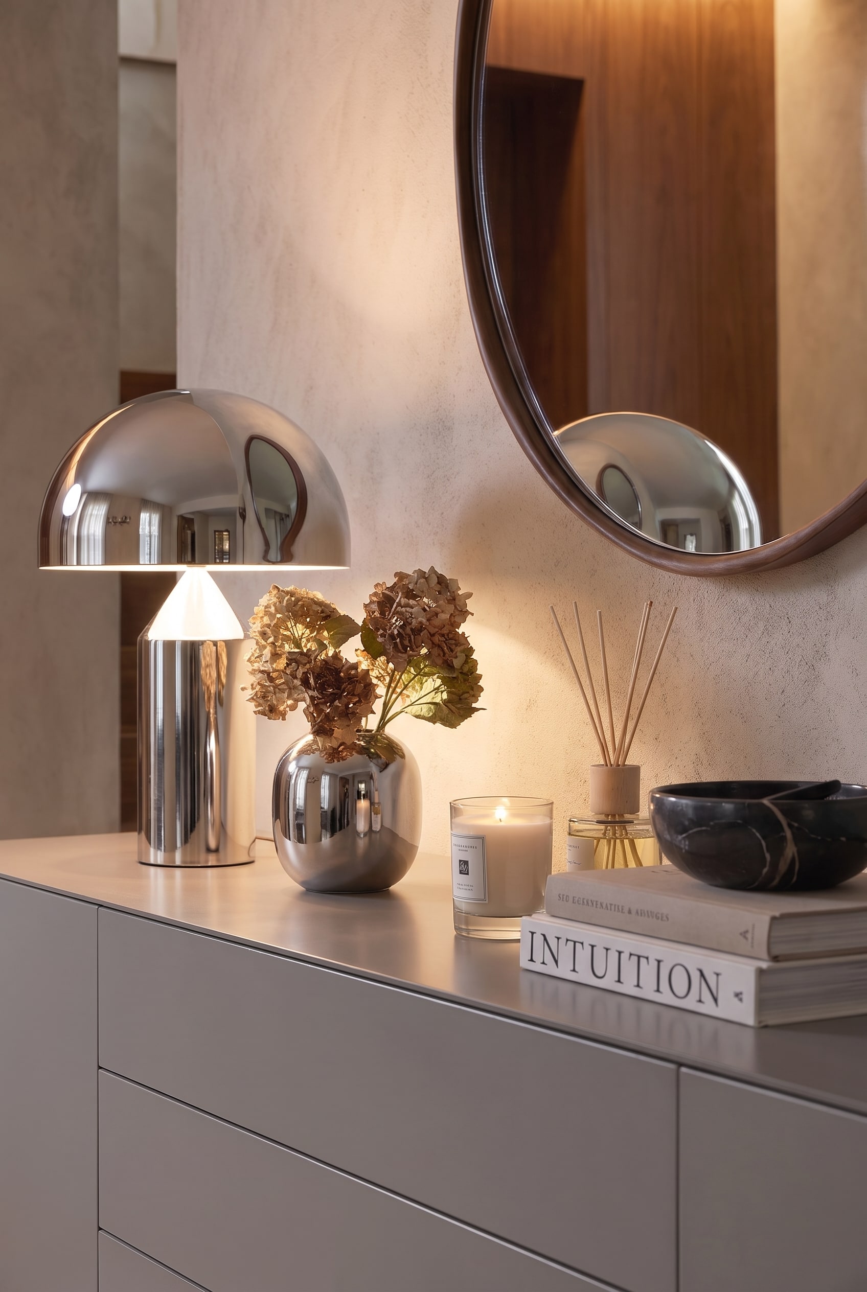 Gros plan sur la décoration : Une lampe chromée brillante, un vase en argent avec des hortensias séchés et une bougie allumée sur une laque grise.