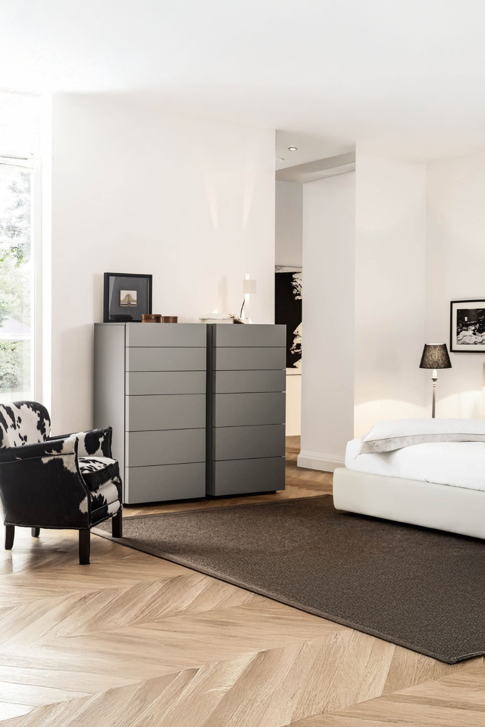 commode &agrave; tiroirs moderne avec fa&ccedil;ades sans poign&eacute;es entre un lit &eacute;l&eacute;gant et un fauteuil extravagant