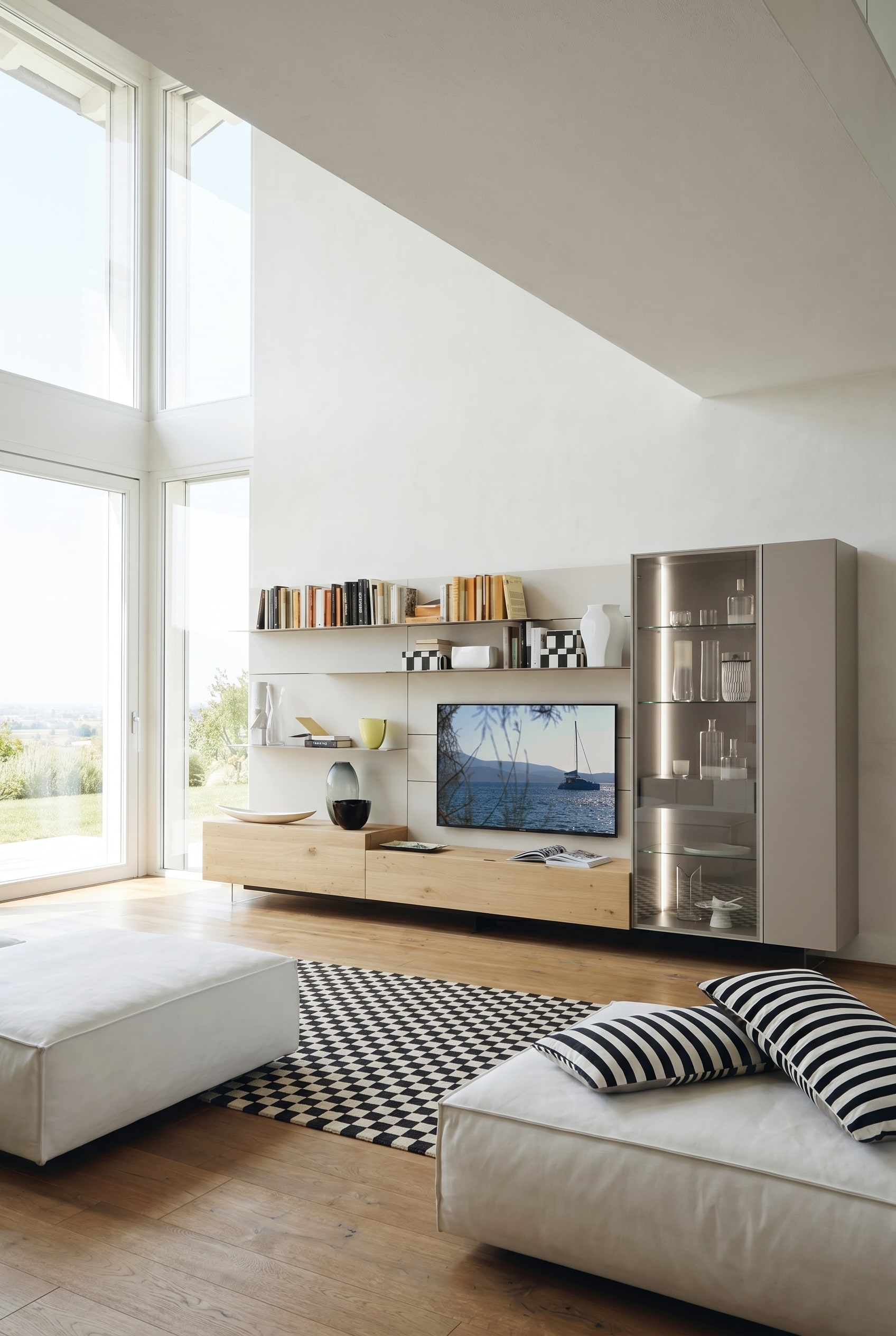 Salon lumineux avec modules de base flottants en chêne clair, étagères blanches et une haute vitrine en verre éclairée chaleureusement