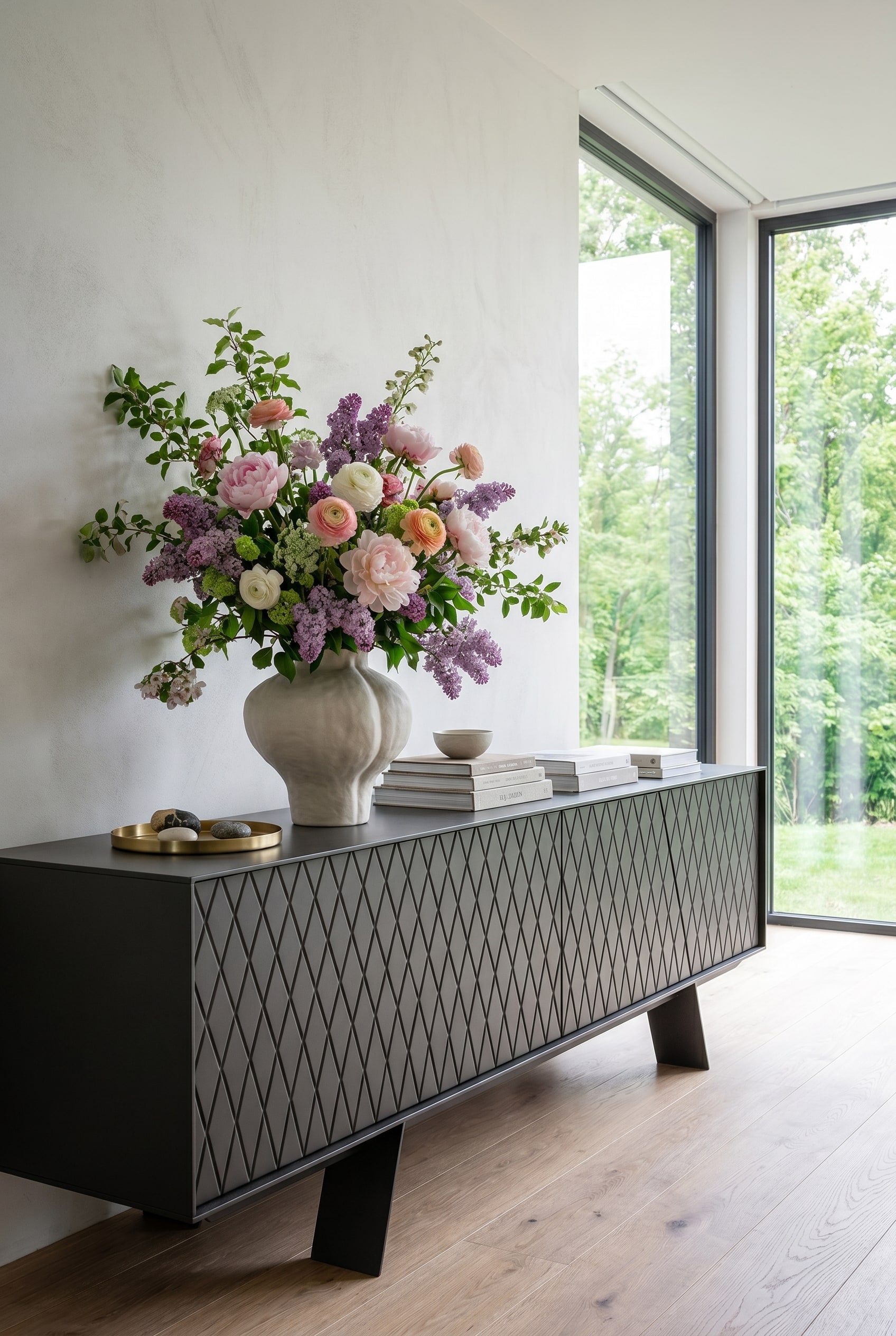 Salon minimaliste avec fen&ecirc;tres du sol au plafond, lumi&egrave;re du jour &eacute;clatante et un &eacute;l&eacute;gant buffet bas sur lequel repose un vase printanier volumineux