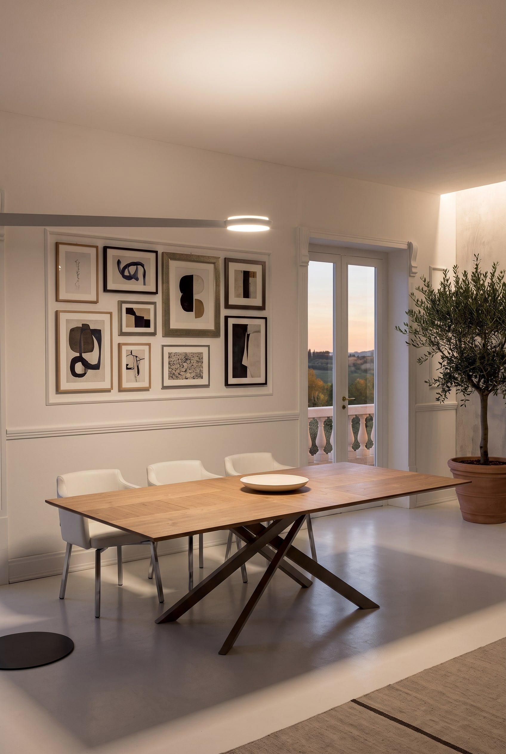Grande table en bois extensible avec piètement métallique croisé dans une salle à manger lumineuse, encadrée par une galerie de tableaux parfaitement alignée