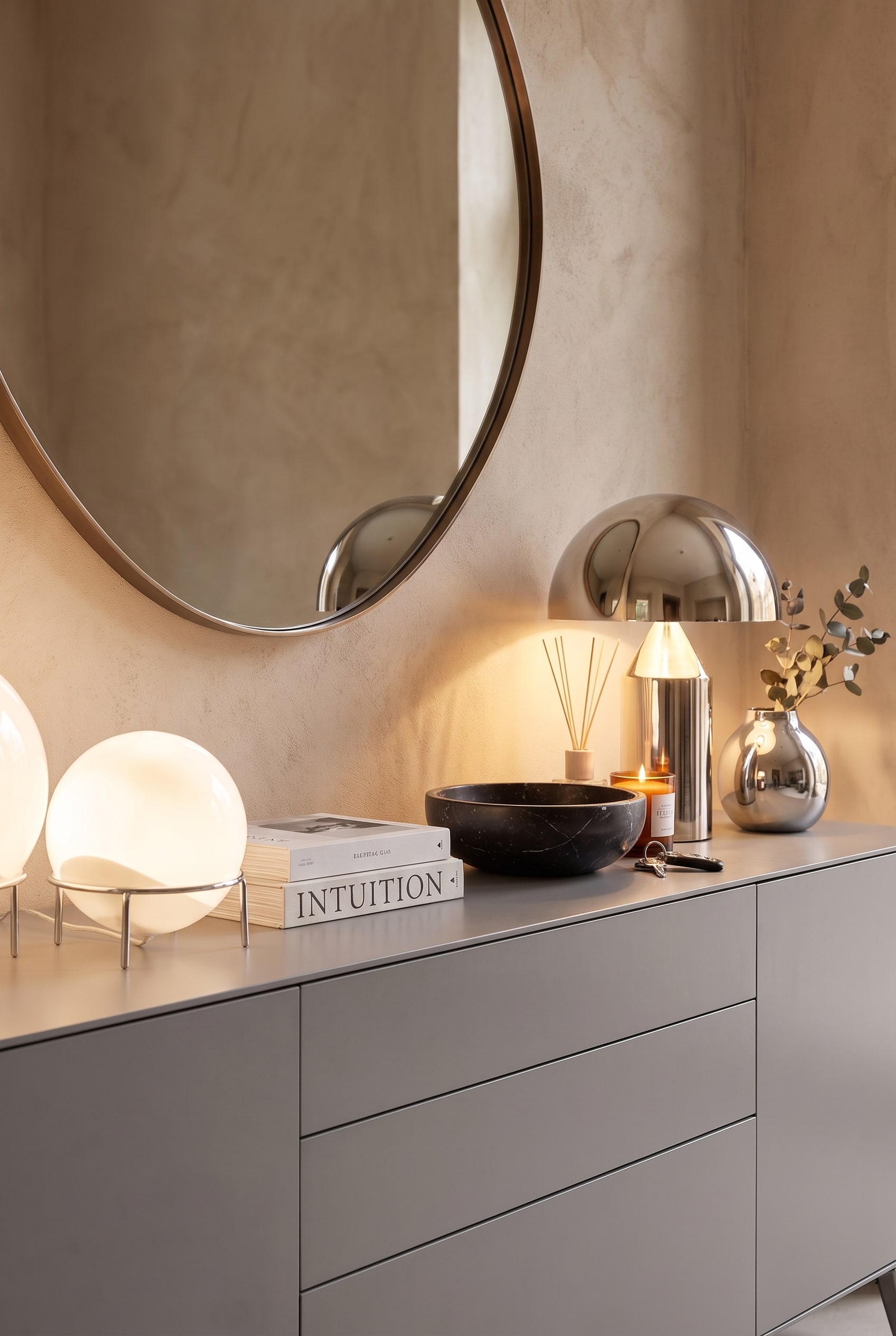 Gros plan sur la d&eacute;coration du buffet avec deux lampes de table rondes et lumineuses, une coupelle en marbre noir et des livres sur une surface mate.