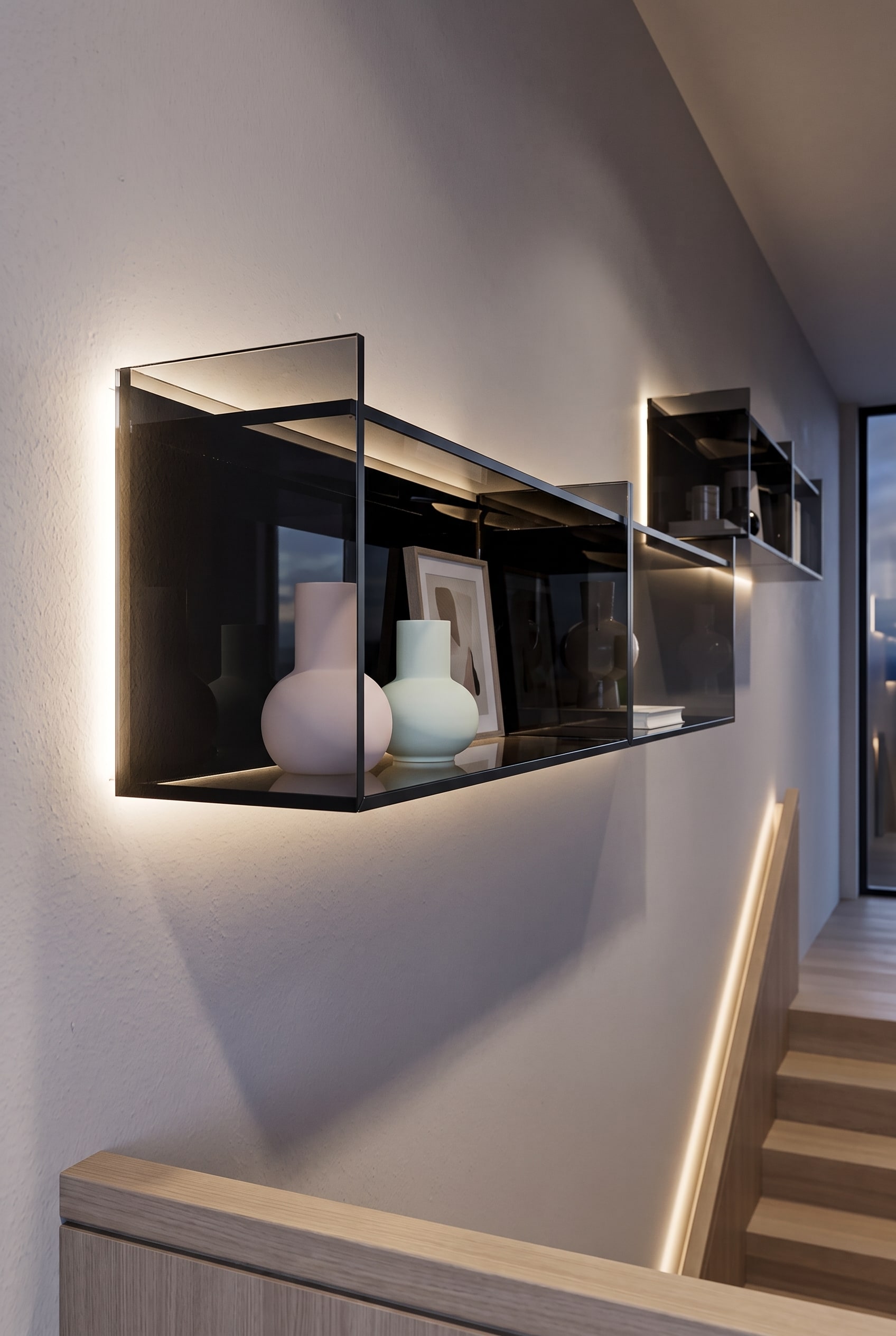 Étagère en verre flottante sur un mur sombre dans l'escalier, garnie de vases clairs et d'objets d'art