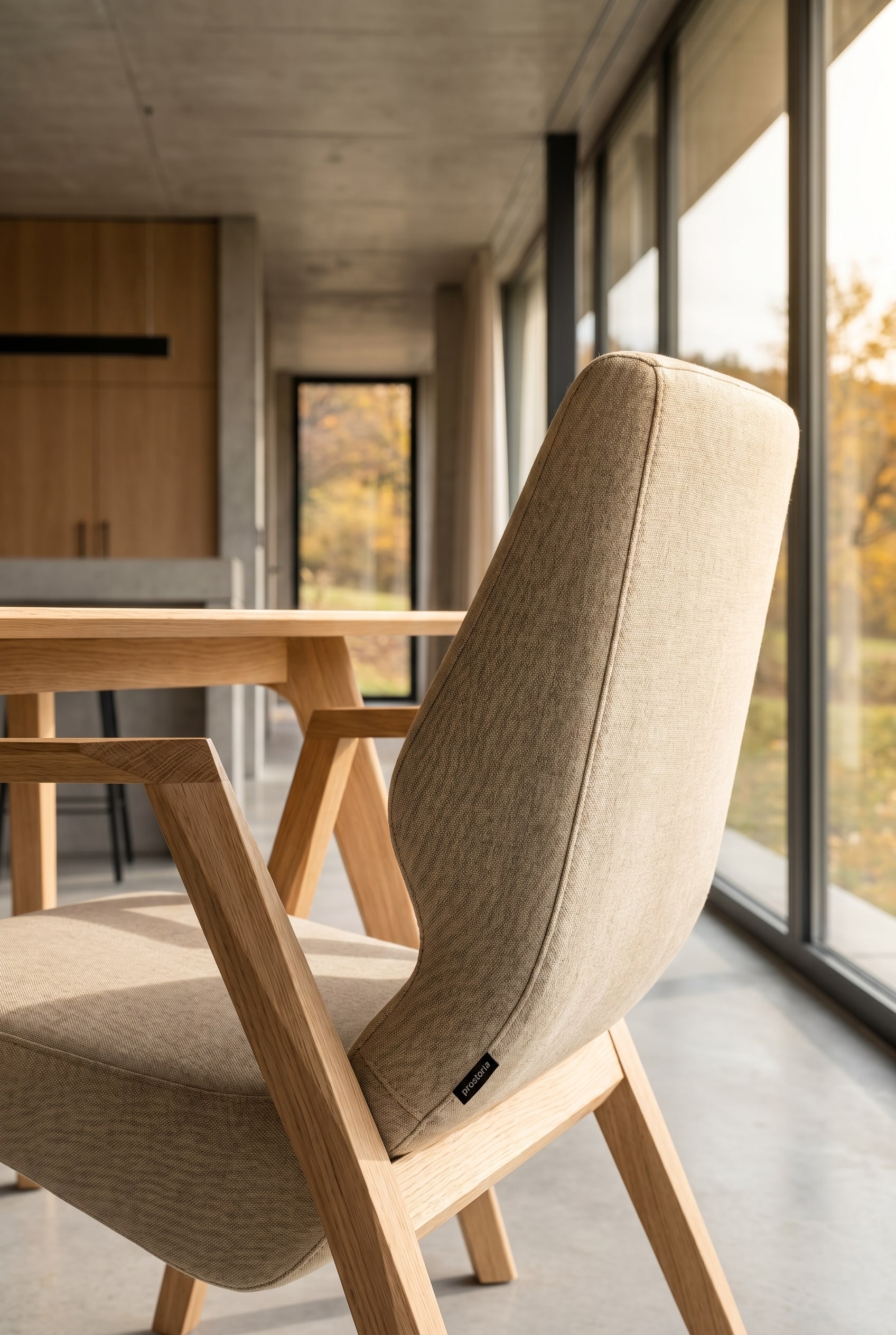 Salle à manger élégante avec un fauteuil Prostoria Oblique avec structure en bois en bout de table devant des fenêtres pleine hauteur