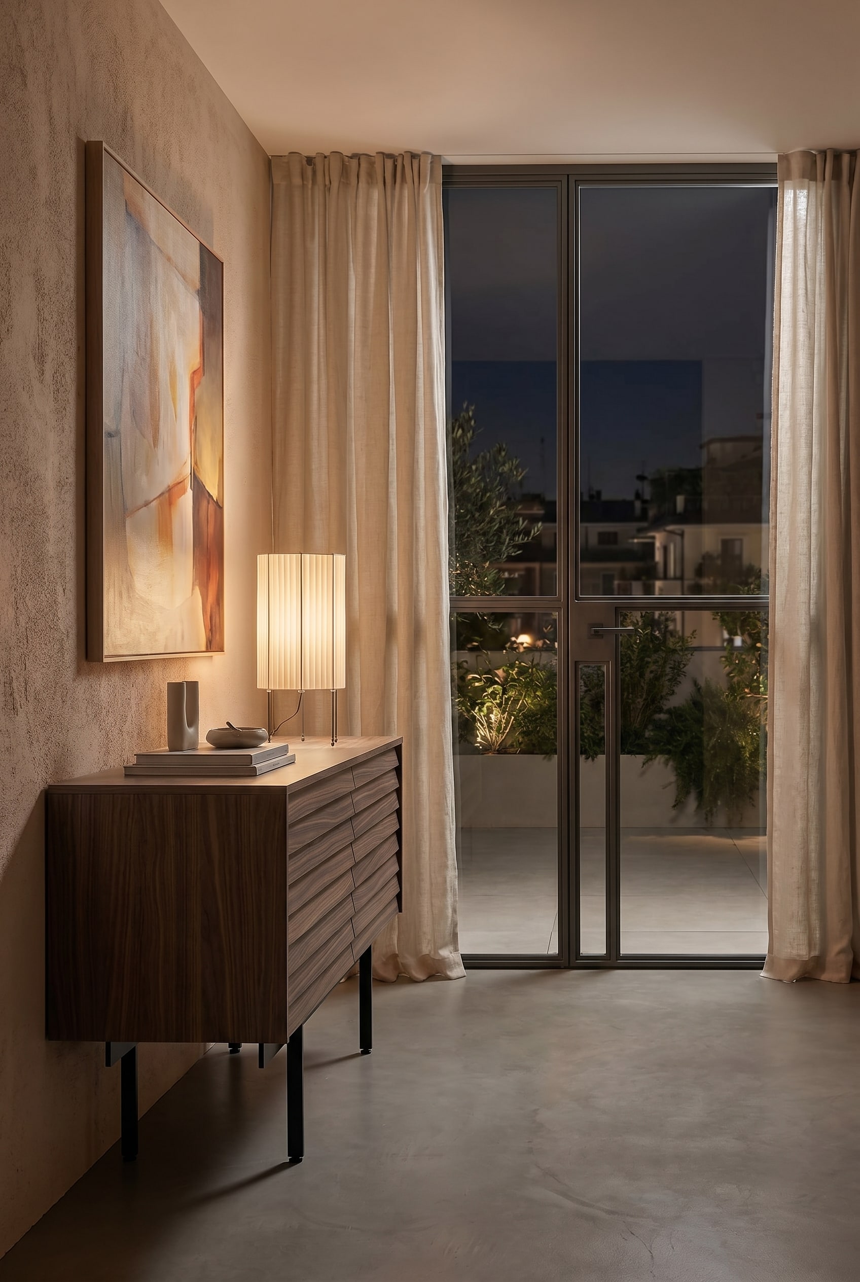 Chambre confortable avec un buffet bas en bois et une lampe de table avec un abat-jour en tissu plissé beige sous une lumière chaude