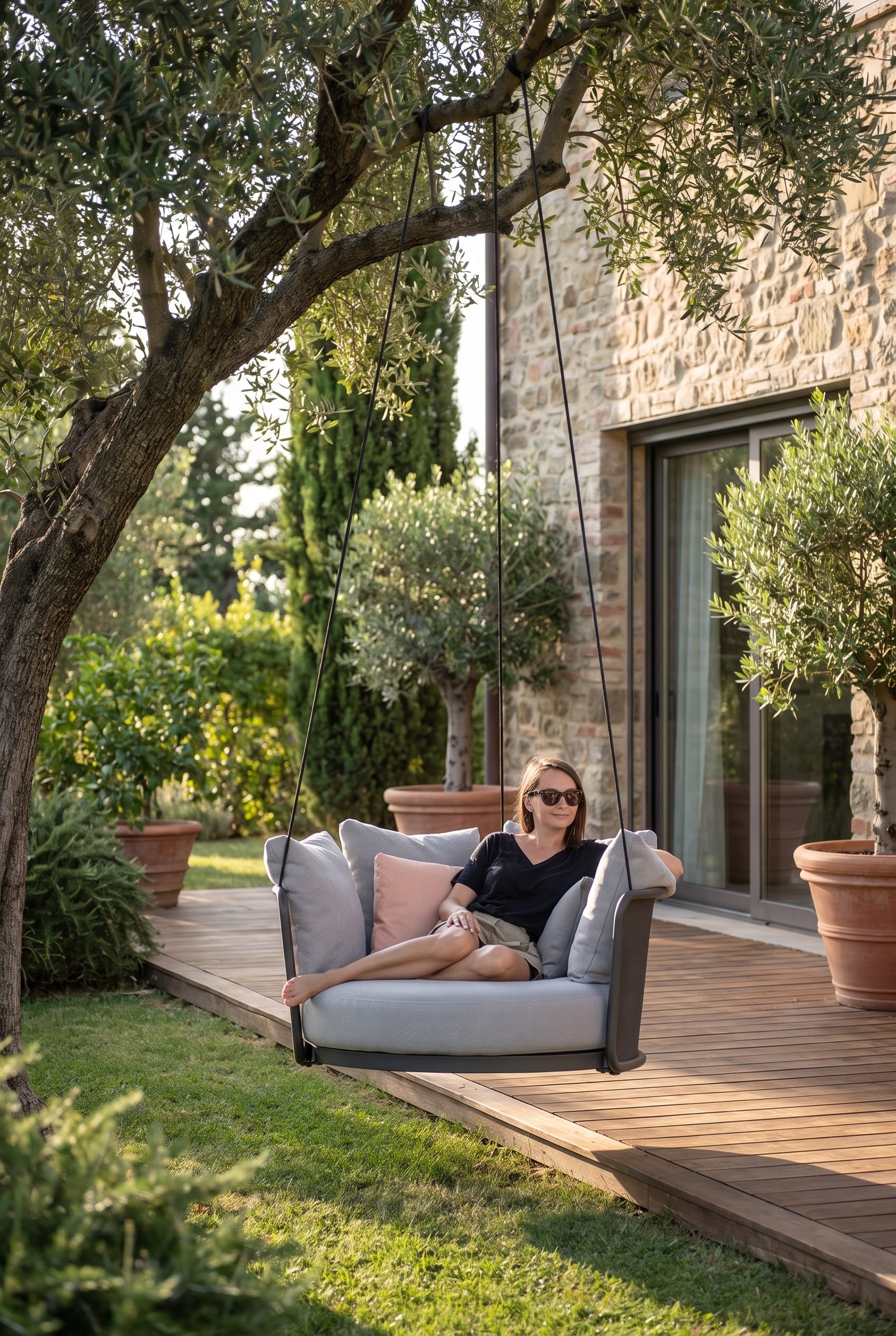 Bord de terrasse vert avec un fauteuil suspendu gris flottant, fix&eacute; &agrave; une structure moderne &agrave; l'ombre fra&icirc;che d'un arbre