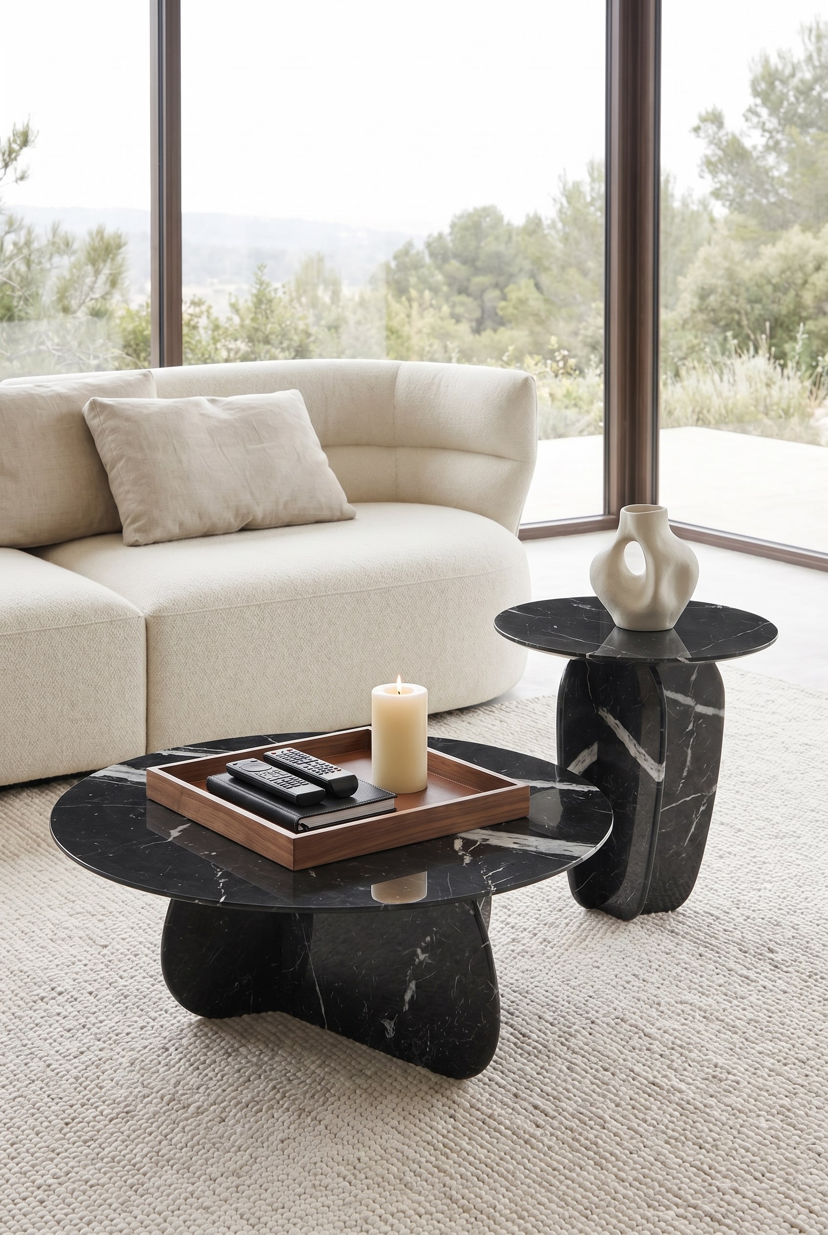 Salon moderne avec table basse en marbre de forme organique, sur laquelle se trouve un plateau en bois carré avec télécommande et bougie pilier