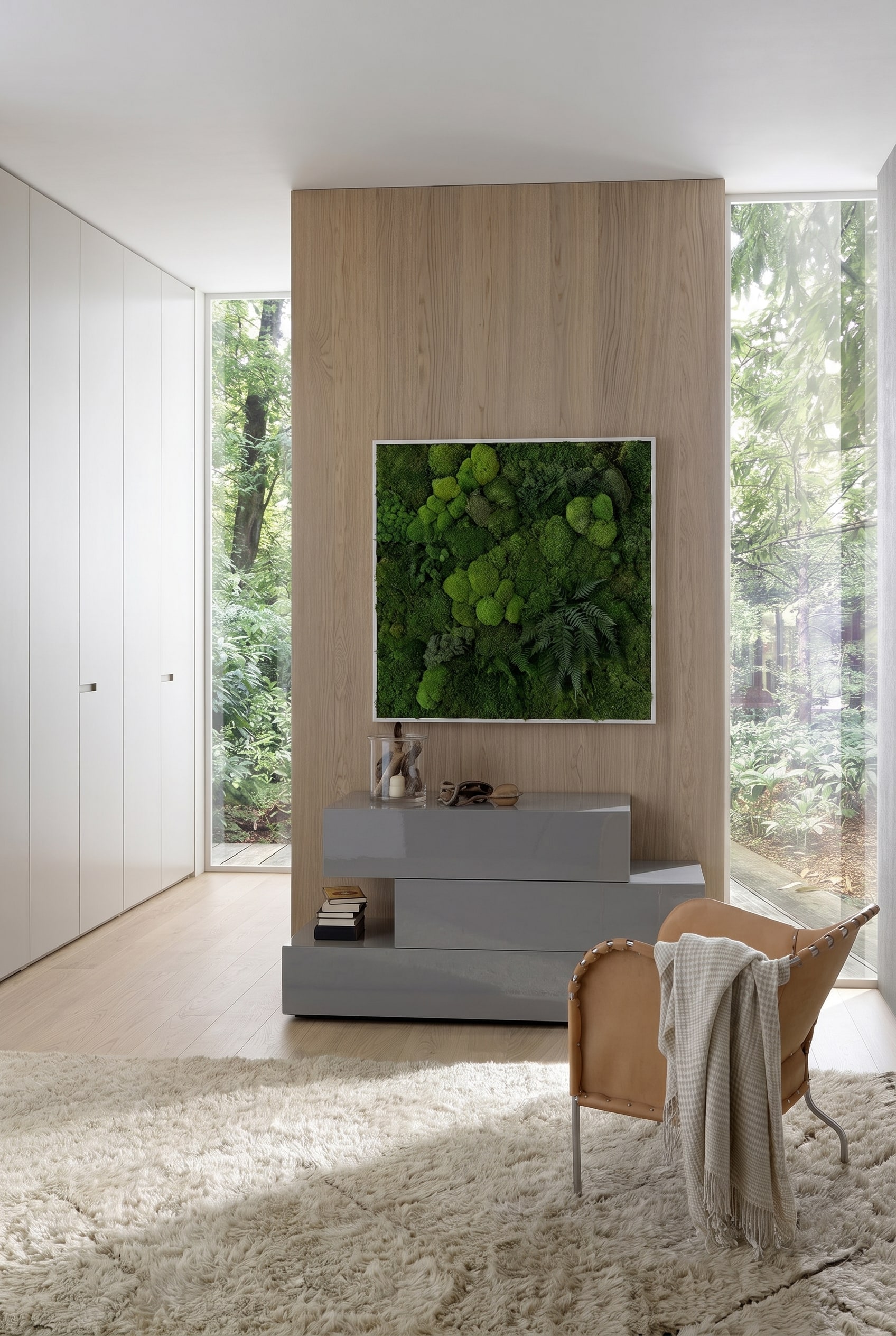 Chambre moderne avec commode grise asym&eacute;trique en laqu&eacute; brillant, surmont&eacute;e d'un tableau de mousse encadr&eacute; et d'un fauteuil en cuir