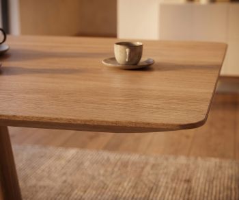 Table de repas mos-i-ko 001 a en chêne clair, zoom sur le coin arrondi du plateau en bois dans une salle à manger moderne.