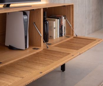 Meuble TV lowboard Punt Malmö en chêne avec porte abattante à claire-voie et rangement pour console dans un salon moderne.